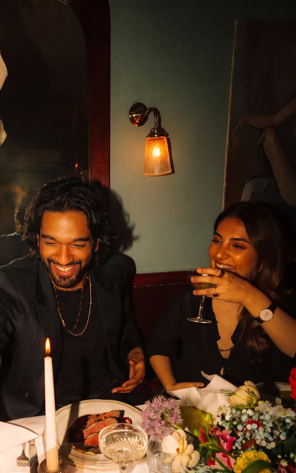 Friends laughing in a booth around a candlelit dinner table