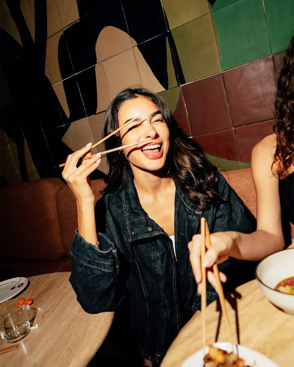 A woman laughing with chopsticks in her hand at dinner